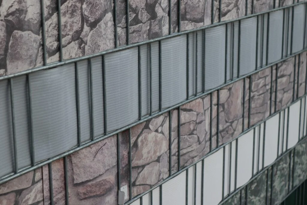 Eine Wand mit abwechselnden horizontalen Reihen von Paneelen; einige Reihen haben ein Steinmuster, während andere hellgraue und weiße vertikale und horizontale Linien aufweisen - perfekt für eine moderne Gartenausstellung.